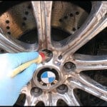 A gloved hand uses a brush to perform car detailing on a BMW wheel rim.