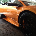 A close-up of an orange sports car with black wheels parked on a brick surface, showcasing its pristine finish thanks to a ceramic coating.