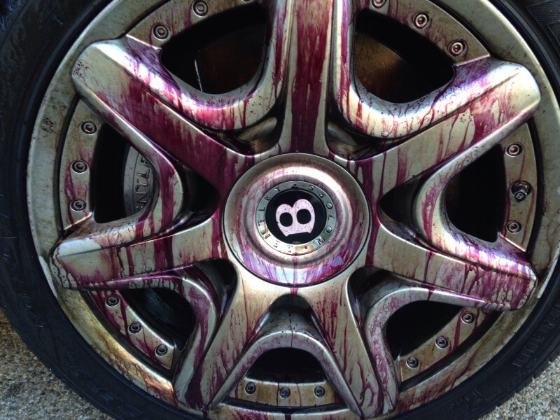 Close-up of a car wheel rim covered in a purple-tinted cleaning liquid, creating a streaky, stained appearance against the metallic surface. This highlights the importance of car detailing to maintain the integrity and appearance of your vehicle.