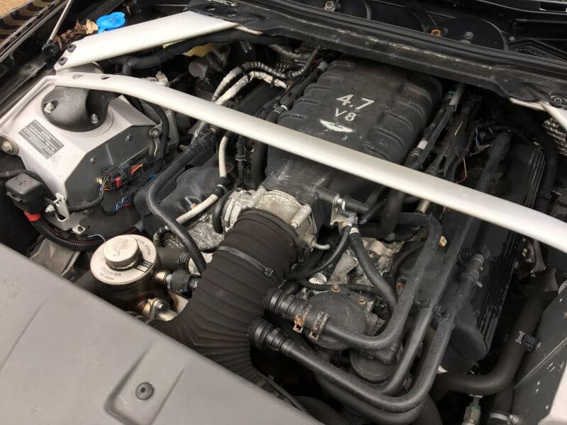 Close-up view of a V8 engine with a 4.7-liter capacity, featuring various components including piping, wiring, and a front strut bar within a car's engine bay after thorough car valeting.