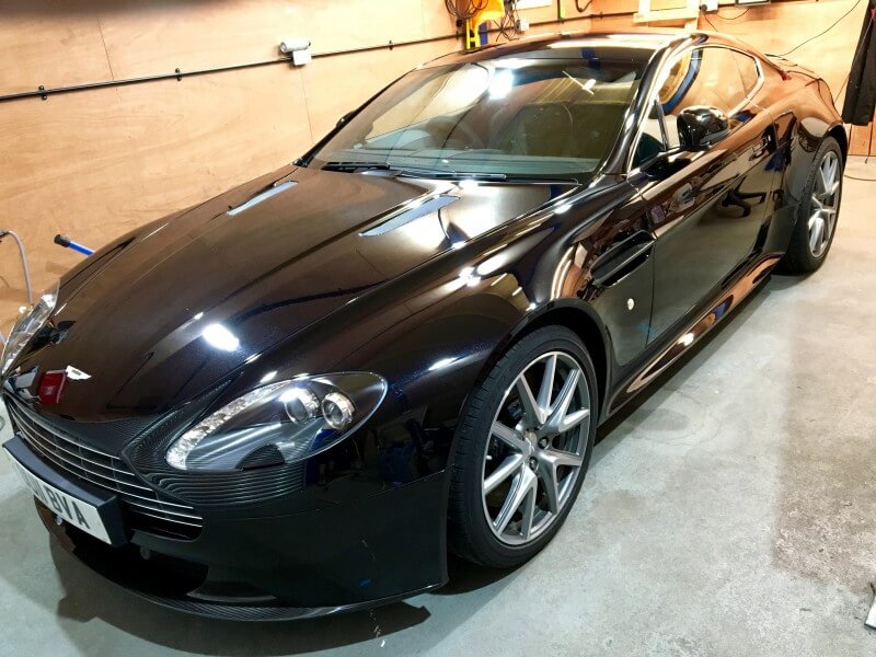 A sleek black sports car with ceramic coating parked in a dimly lit garage.