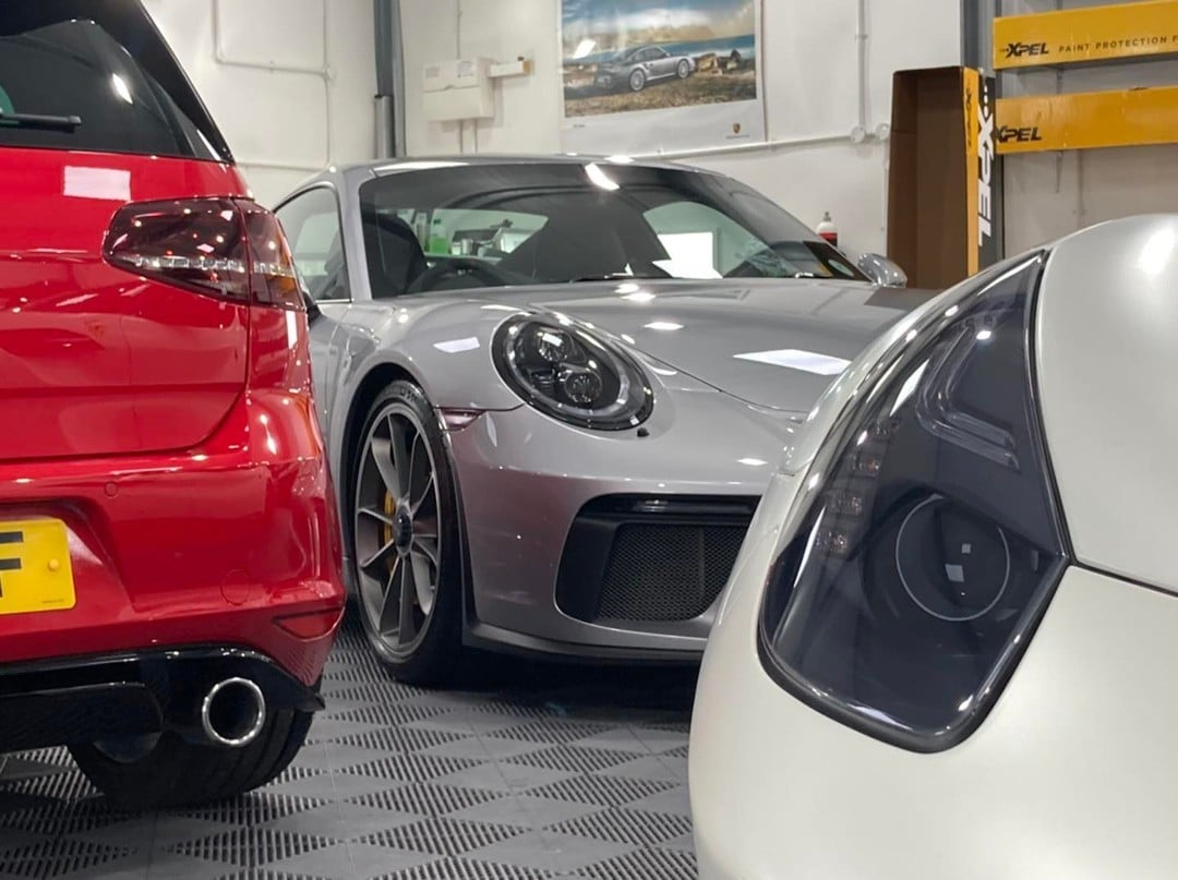 Close-up view of three luxury cars in a garage, featuring a red car on the left, a silver sports car in the center with impeccable car detailing, and a white car on the right.