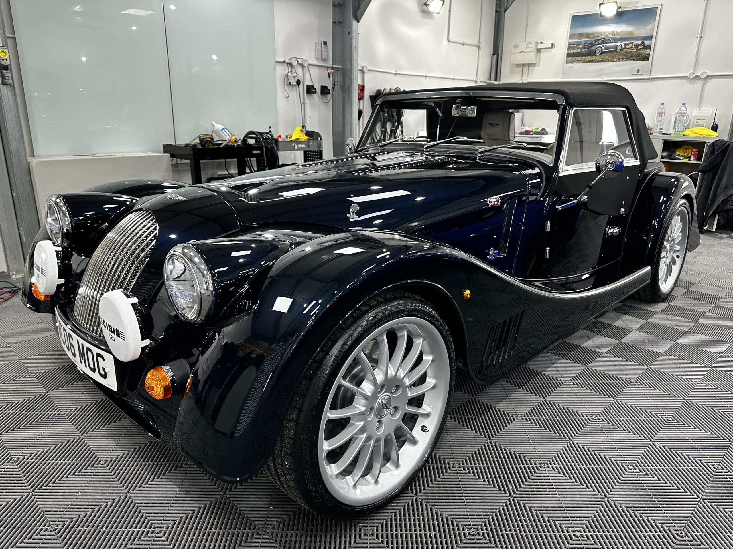 A black vintage-style convertible car with a soft top is parked in a modern garage with checkered flooring, freshly detailed by a top-notch car valeting service.