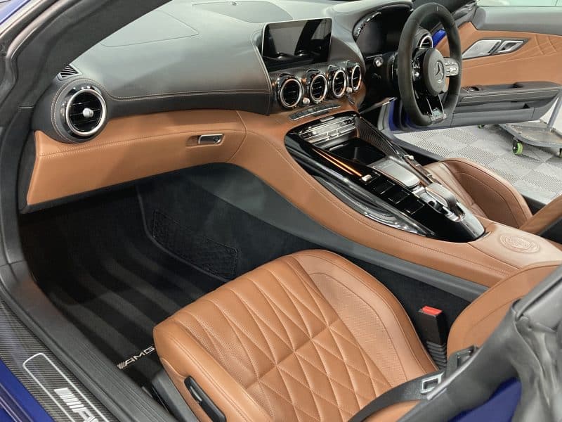 Interior of a luxury sports car with brown leather seats, a sleek dashboard featuring multiple air vents and digital displays, and a central console with glossy black finish and various controls. For added protection, consider applying paint protection film to maintain its pristine condition.