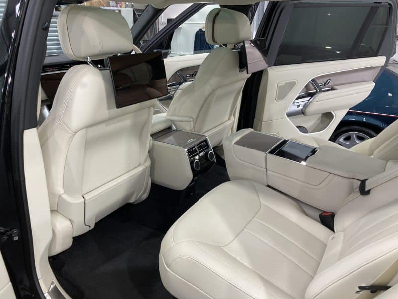 Interior of a modern luxury SUV with white leather seats, rear entertainment screens, and a central control console featuring car valeting services.