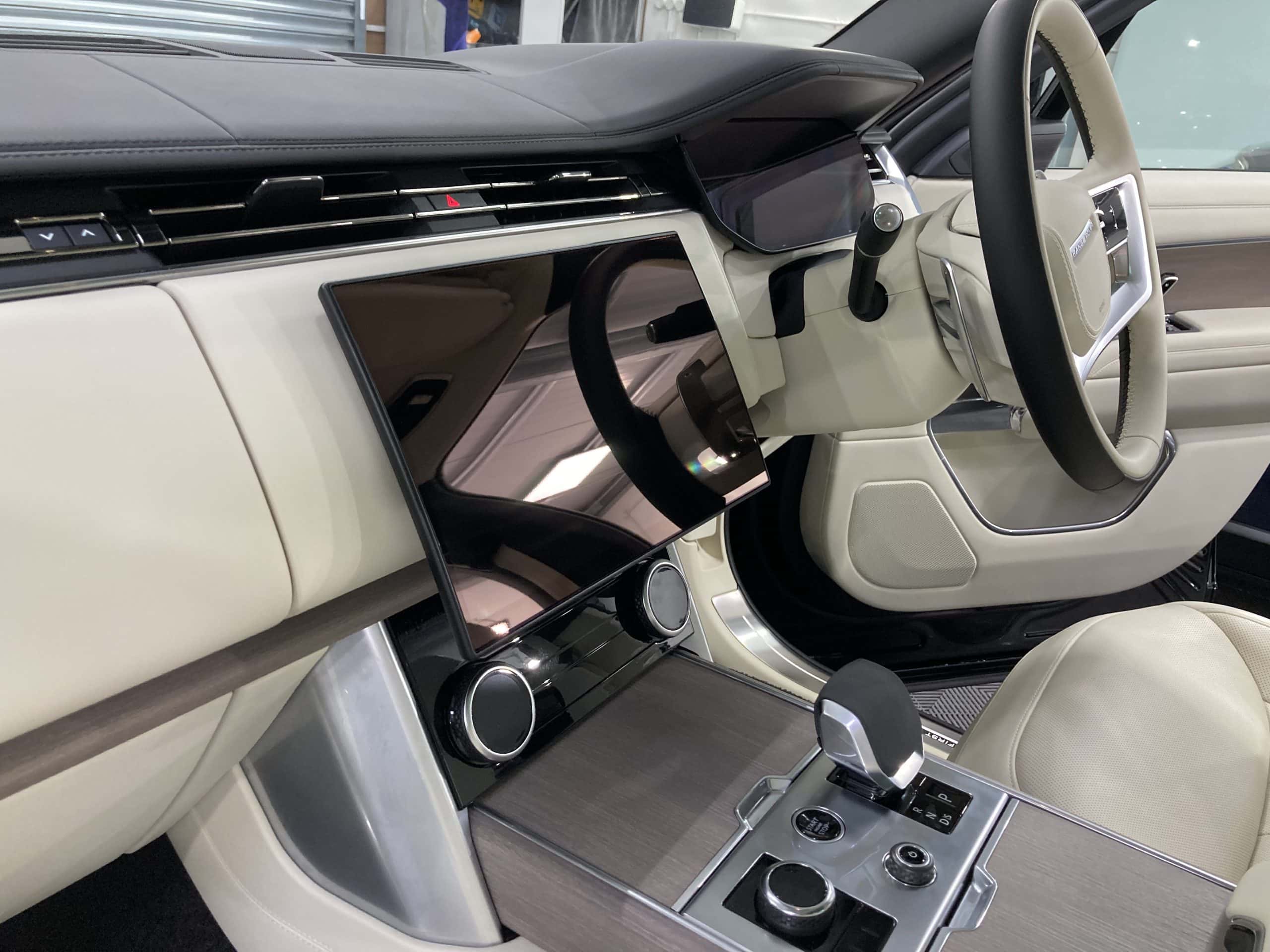 Interior of a modern car showcasing a sleek dashboard with a digital display, center console with controls, and a steering wheel. The car detailing highlights the luxurious finish. The color scheme is predominantly light beige and black.