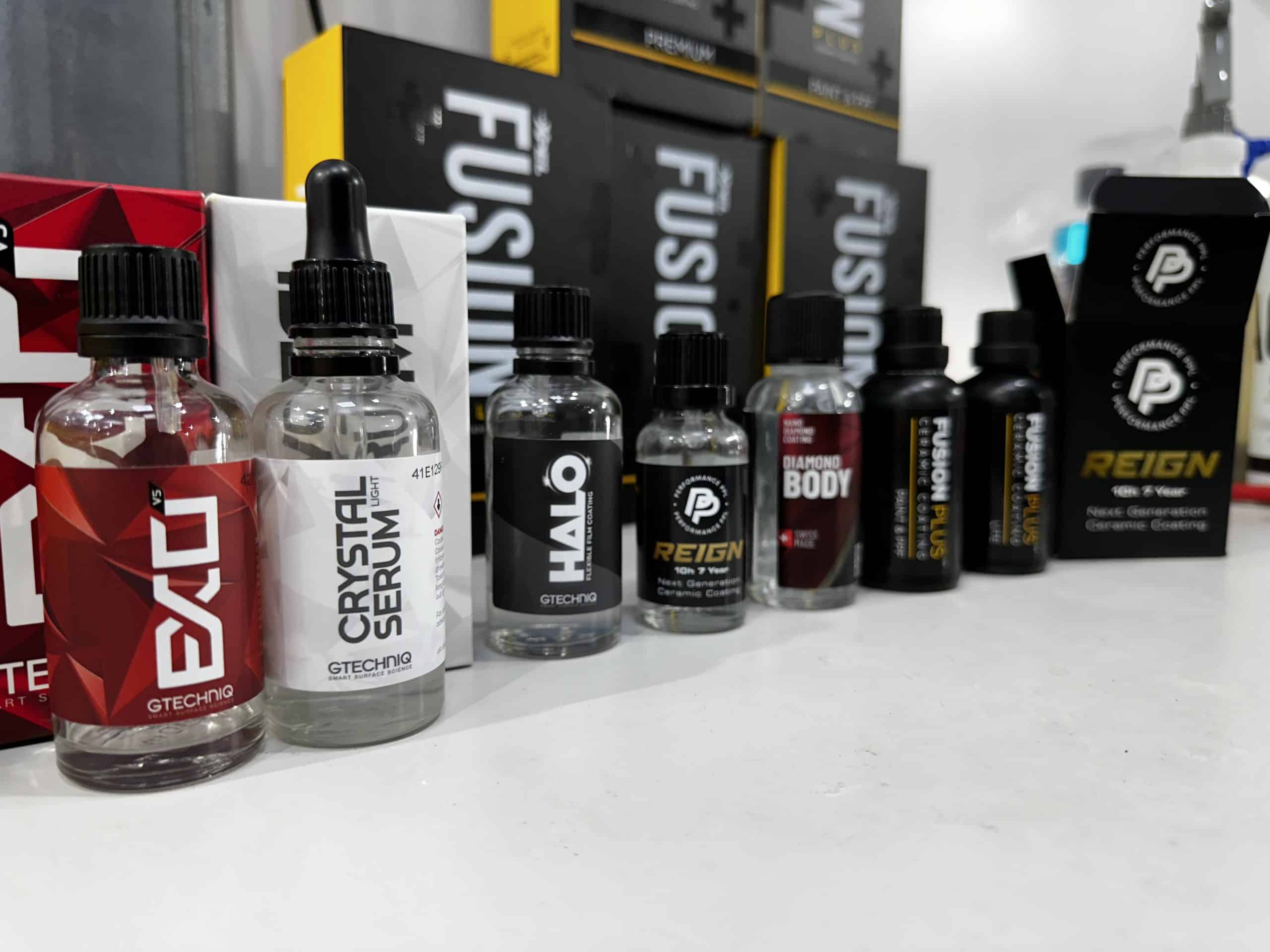 Various car care product bottles—including Gtechniq EXO, Crystal Serum, and more—displayed in a row on a countertop. These essentials are perfect for car detailing and offer top-notch ceramic coating solutions.